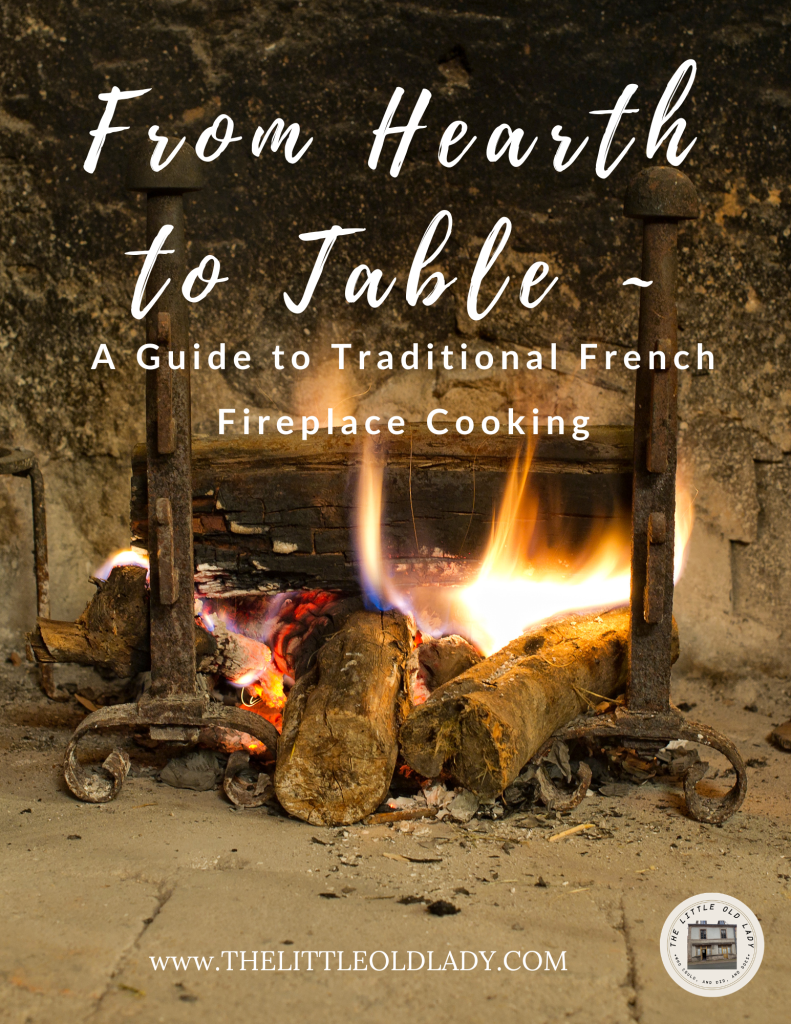 Cover of From Hearth to Table: A Guide to Traditional French Fireplace Cooking, showing a wood fire burning between two iron andirons in an old stone hearth
